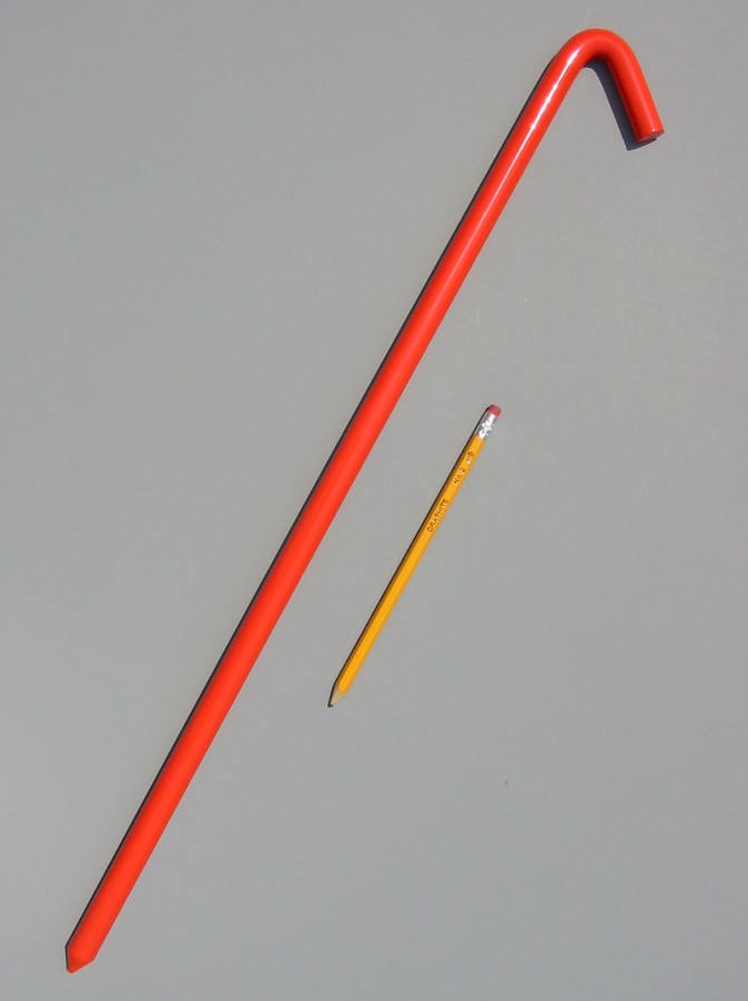24 inch metal hook style tent stake in safety orange color and a pencil for scale